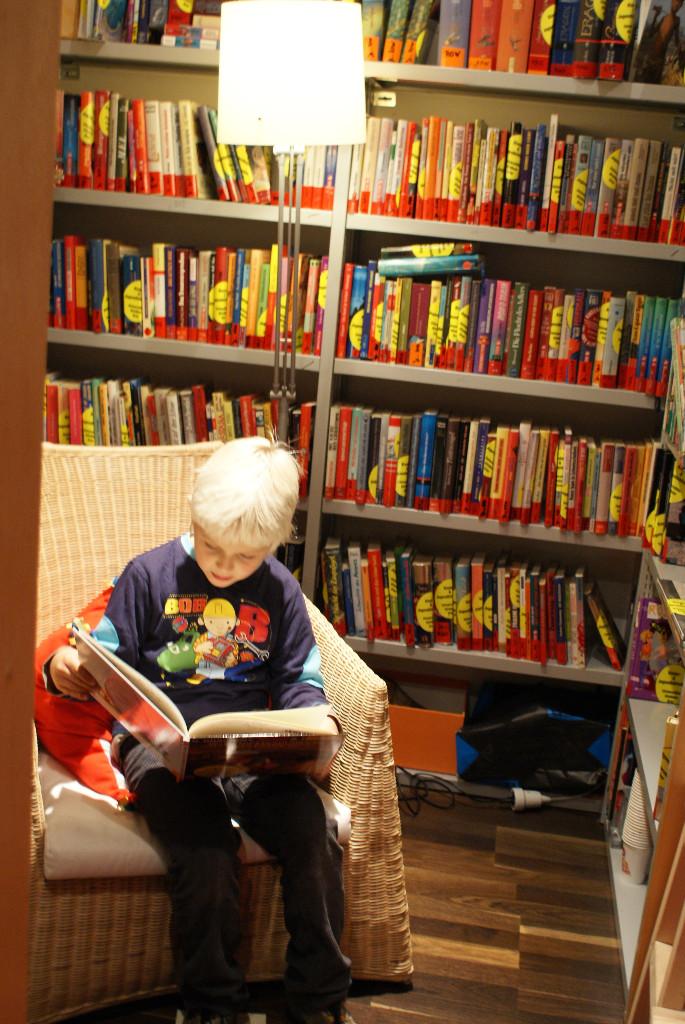 Junge liest ein Buch vor Bücherregal